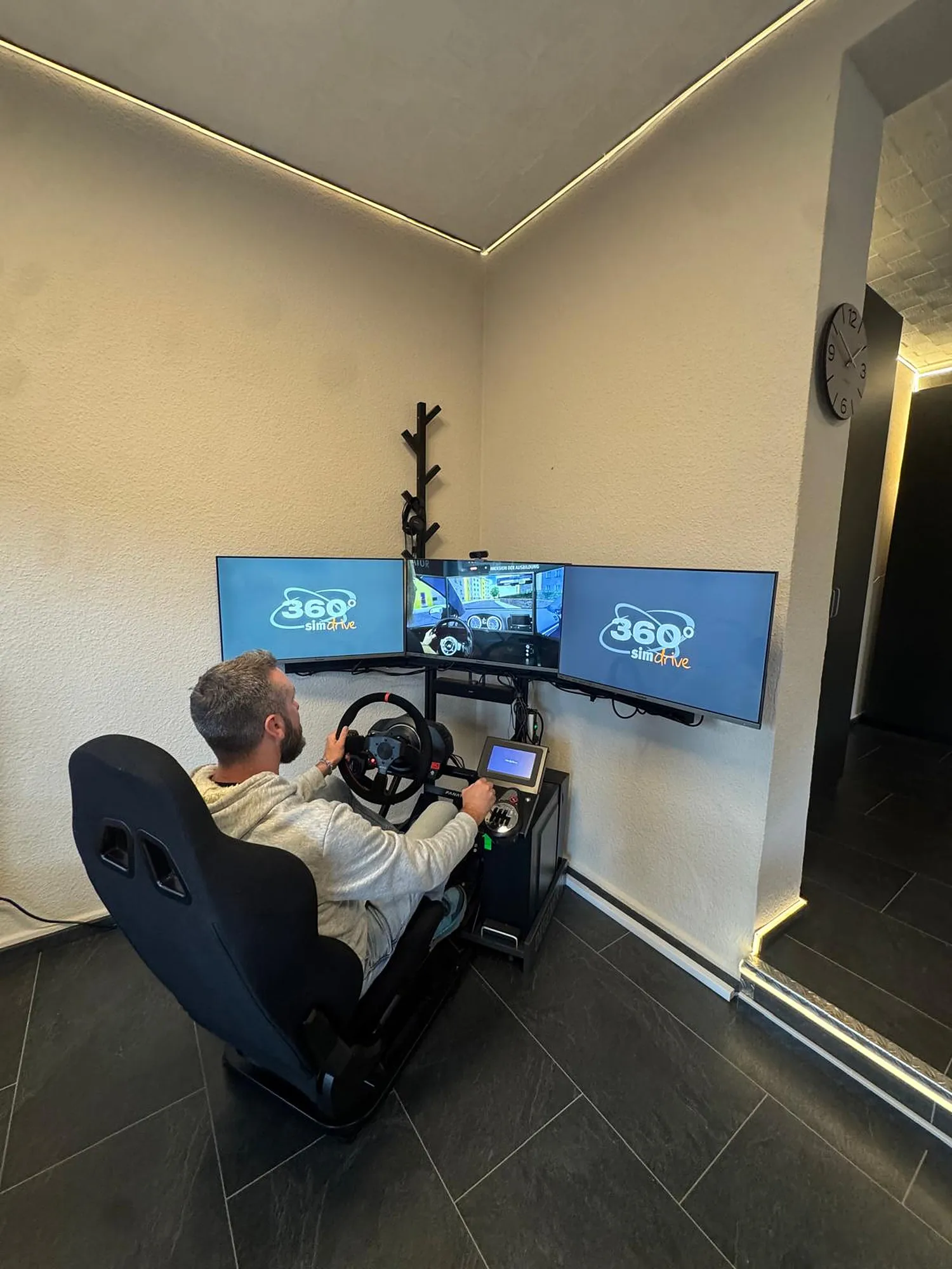 Fahrschüler am Fahrsimulator mit Lenkrad, Schaltung und drei Bildschirmen